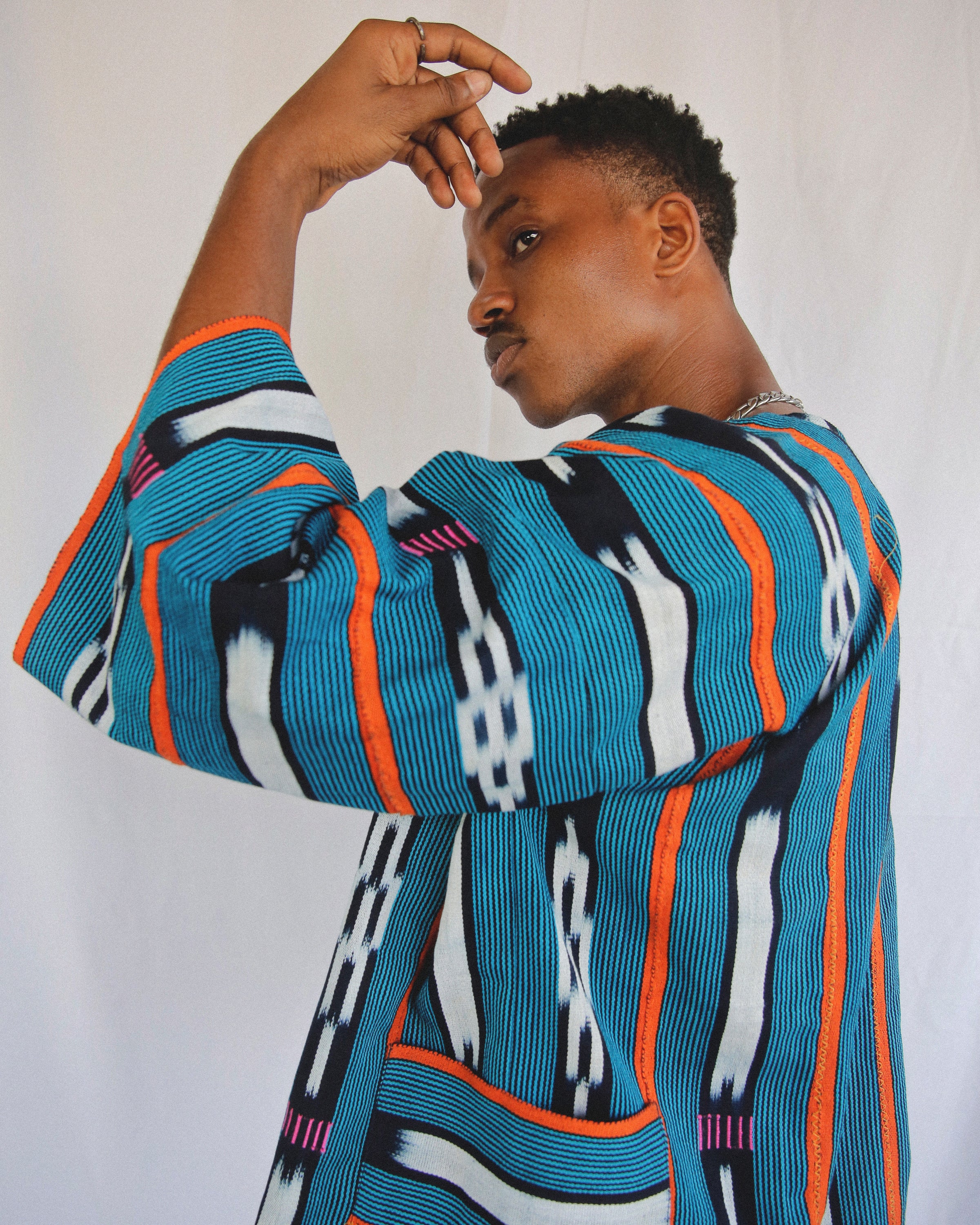 African man in aqua blue Baule textile cloak with orange, white and Navy colors with side pockets
